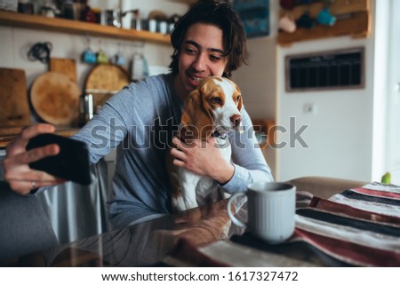 young man with his dog taking picture in kitchen at home, morning scene
