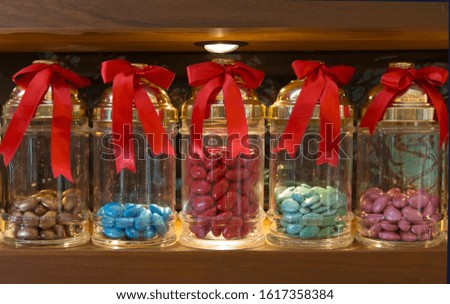 Big glass jars with red ribbons and colorful candies. Sweets, surprises, patisserie, decoration concepts. Horizontal close-up.