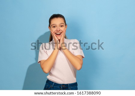 Astonished, wondered. Caucasian teen girl's portrait on blue background. Beautiful model in casual wear. Concept of human emotions, facial expression, sales, ad. Copyspace. Looks cute, happy.