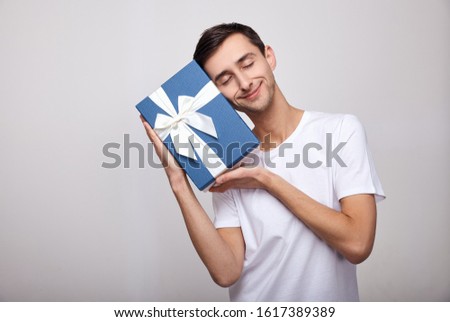 Adorable photo of attractive man with beautiful smile leaning his head to birthday present box isolated over white wall. Portrait of cheerful candid lover man hold big wish gift box. Copy space.