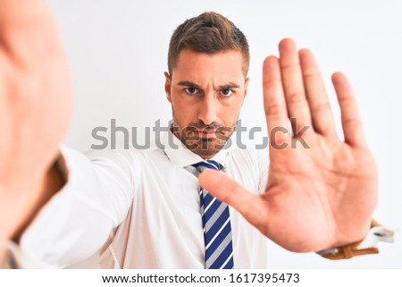 Young handsome business man taking selfie using smartphone over isolated background with open hand doing stop sign with serious and confident expression, defense gesture