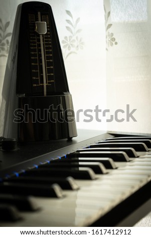 metronome on top of a piano illuminated by the light coming through the window through the curtain, natural white background, selected focus, music concept
