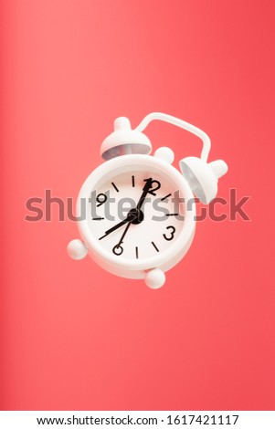 White retro style alarm clock in levitation isolated on pink background. Royalty-Free Stock Photo #1617421117