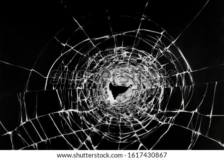 Cracks on broken glass. The window is damaged by a shot from a firearm. Transparent windscreen of a car with a hole after the shots.