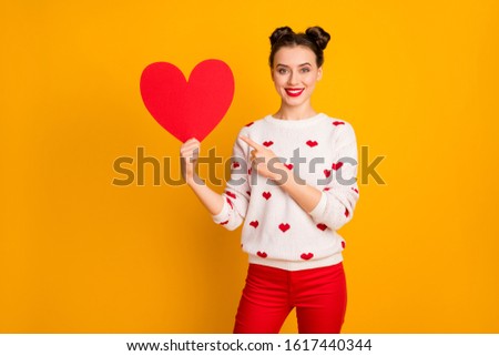 Photo of pretty affectionate lady hold paper heart show date postcard indicating finger promotion wear white red hearts pattern pullover pants isolated yellow color background