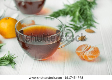 Tea in a glass cup on a light wooden background. Black tea with rosemary and tangerines. Space for text.