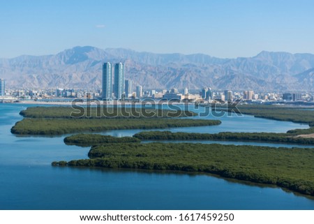 Aerial view of Ras al Khaimah, United Arab Emirates north of Dubai, looking at the city, Hajar mountains - Jebal Jais - and the Mangroves along the Corniche. Royalty-Free Stock Photo #1617459250