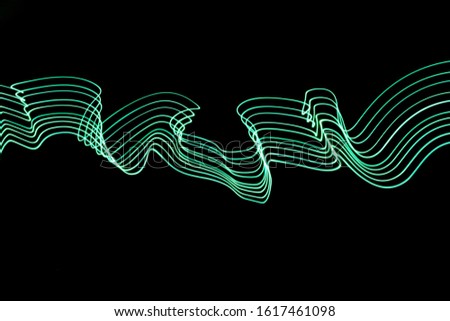 Long exposure light painting photo, vibrant neon green color in abstract swirls pattern against a clean black background.  Light painting photography.