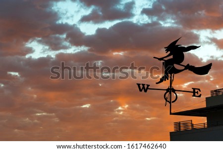Silhouette of weather vane with witch flying on broomstick above colorful and dramatic sunrise, digital composite image