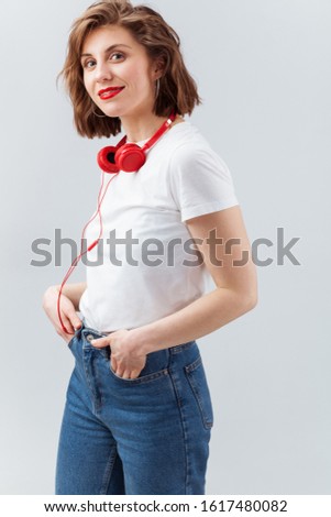 Lovely woman with red earphones in casual clothes against light background