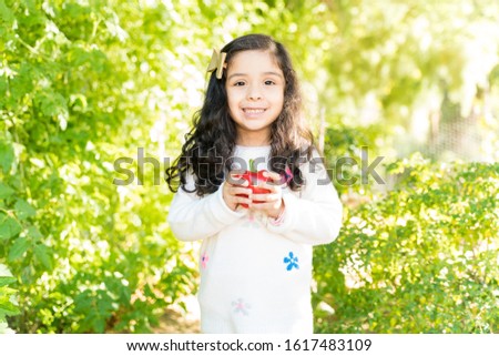 Cute smiling Hispanic girl holding fresh bell pepper while standing at farm