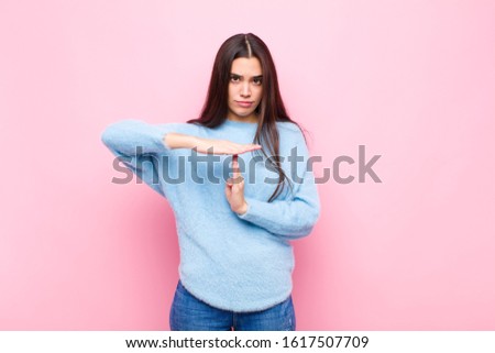 young pretty woman looking serious, stern, angry and displeased, making time out sign against pink wall