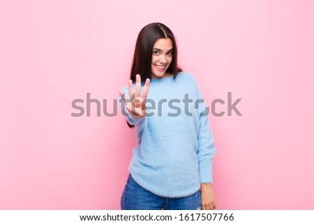 young pretty woman smiling and looking friendly, showing number four or fourth with hand forward, counting down against pink wall