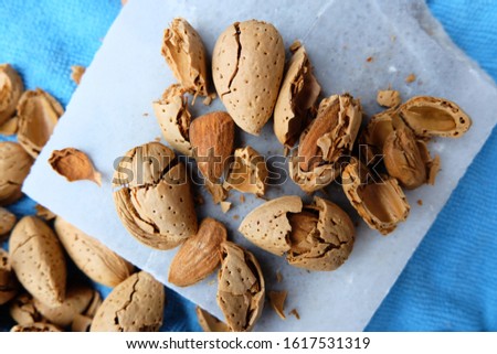 Raw Almond shell background with nut shell cracker hammer. Basic tools for shelling almonds on a colorful blue background outdoors. female hand cracking and picking up almond. 