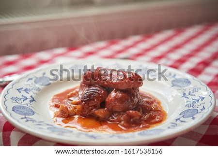 Close up Picture of warm, tasty czech traditional specialty, small sausages baked in dark beer sauce made from czech beer, tomato sauce, garlic, onion and chily served on rustic plate on the table. 