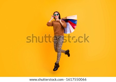 Full body profile photo of pretty lady jumping high carry many packs shopper self-confident person wear fluffy sweater leopard trousers footwear isolated yellow color background