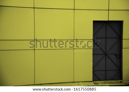 A black closed door with yellowish exterior wall of a house