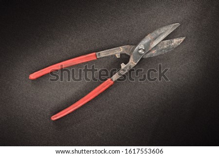 old rusty metal scissors with red handles on a black background