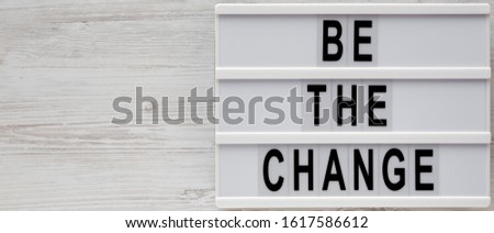 'Be the change' words on a modern board on a white wooden surface, top view. Overhead, from above, flat lay. Space for text.