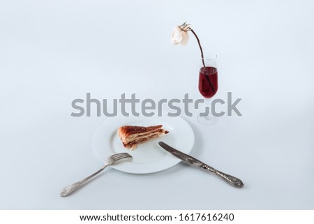 White plate with a piece of pie on it, fork, knife and glass of champagne with faded rose on a white background.