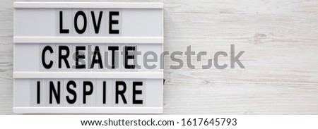 'Love create inspire' words on a lightbox on a white wooden background, top view. Overhead, from above, flat lay. Copy space.