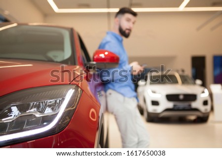 Selective focus on car lights, man using smart phone, leaning on a car on the background. Technology, buying auto concept