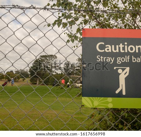 Caution Stray golf balls sign clipped onto a wire mesh fence at a golf course