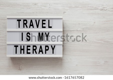 'Travel is my therapy' words on a lightbox on a white wooden surface, top view. Overhead, from above, flat lay. Space for text.