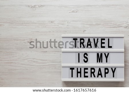 'Travel is my therapy' words on a lightbox on a white wooden background, top view. Overhead, from above, flat lay. Copy space.