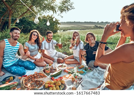 Woman clicking a photo of her friends at a picnic on a sunny day.