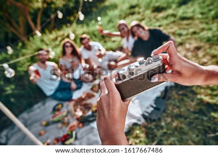 Woman taking picture of her friends by vintage camera on picnic at summer park. Selective focus
