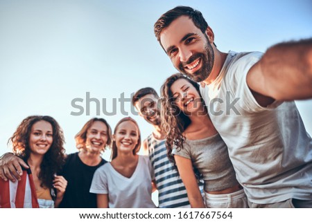 Group of happy teenage friends taking selfie on nature. Young woman with american flag background. Country, patriotism, independence day, people and technology concept. Selective focus.
