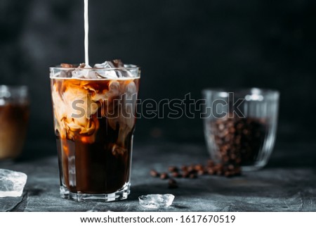 Milk Being Poured Into Iced Coffee on a dark table Royalty-Free Stock Photo #1617670519