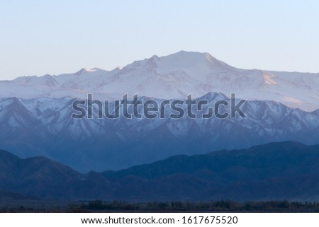 Mountain range with snow in different shades of blue at Issyk Kul region in Kyrgyzstan. Low contrast scene with negative space available for text. Empty sky and faint light.