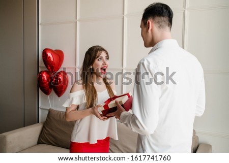 happy woman receives gift from man with red heart shaped balloons at home