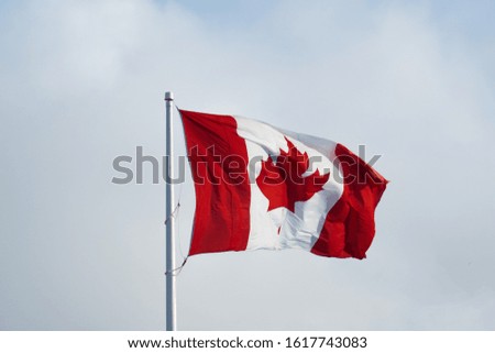 the Canadian flag flying in a breeze with light clouds