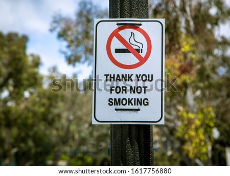 Sign on lamp post that reads “Thank You For Not Smoking” with trees diffused inthe background