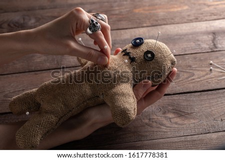 Voodoo doll on a wooden background with dramatic lighting. The concept of witchcraft and black art. Burlap doll on a wooden background. Hands stick pins into a doll.