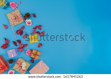 various of gift box, small pink rose, dried red leaves and pine cone put on the left of picture and space on the right on blue background