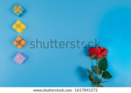 four gift box put on the left of the picture and an artificial red rose on the right on blue background