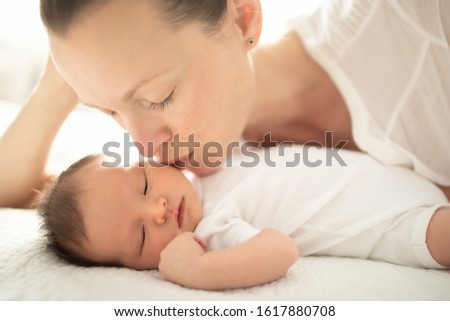 Mother kissing new born baby girl on the cheek. 