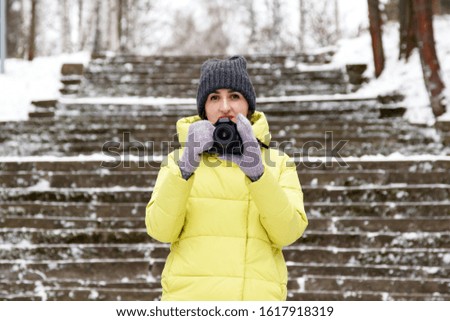 Young woman with a camera in a winter park on a background of stone stairs. A girl photographer holds a camera in hand and takes a picture. Women hobbies Copy space