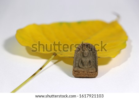 Small buddha amulet with yellow sacred fig or Bodhi leaf on white floor. Use for An anchor to your heart.