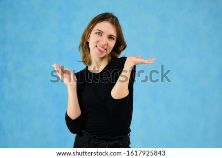 Studio portrait of a pretty blonde girl in a black T-shirt on a blue background with bright emotions. A universal concept, the picture is suitable for any topic.