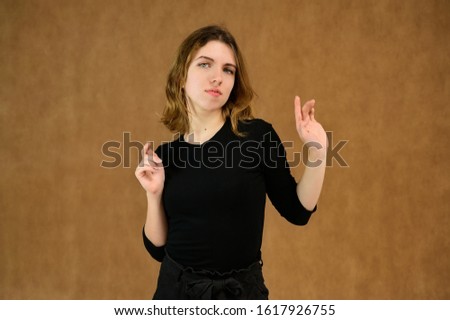 Studio portrait of a pretty blonde girl in a black T-shirt on a beige background with bright emotions. A universal concept, the picture is suitable for any topic.