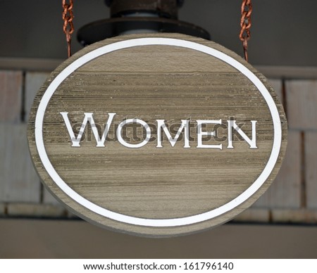 A round wooden sign that reads Women