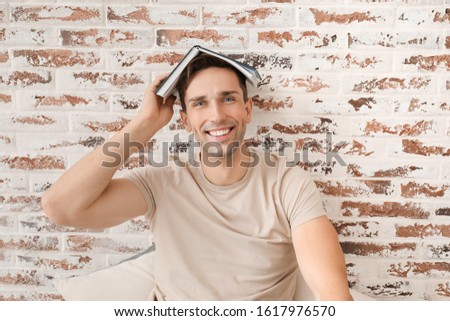 Handsome young man with book near brick wall