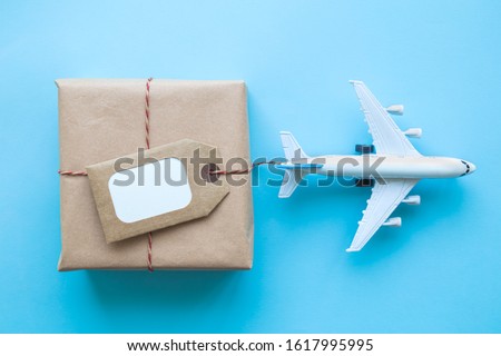 Flat lay of wrapped package with blank tag and airplane model on pastel blue background. Shipping logistics transport minimal creative concept. Royalty-Free Stock Photo #1617995995