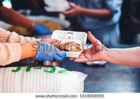 The hands of the poor handed a plate to receive food from volunteers to alleviate hunger, the concept of helping the homeless.