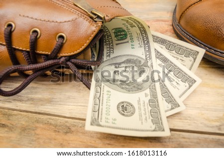 Concept photo of brown leather men's shoes, with dollars inside the shoes on a wooden background
